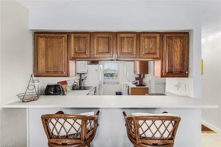 Kitchen featuring light countertops, a kitchen bar, white appliances, and brown cabinetry