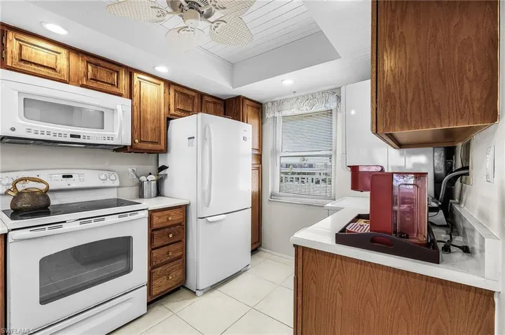 Kitchen featuring white appliances, light countertops, light tile floors, brown cabinetry, and recessed lighting