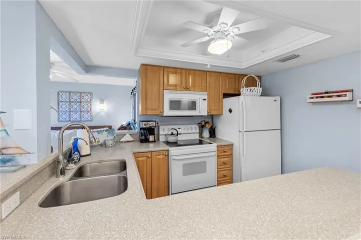 Kitchen featuring a ceiling fan, white appliances, a tray ceiling, a peninsula, and wood finish cabinets
