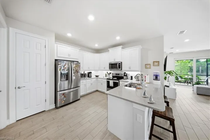 Kitchen featuring appliances with stainless steel finishes, a breakfast bar area, a peninsula, white cabinets, and light stone countertops
