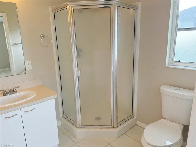 Bathroom featuring tile flooring, vanity, toilet, and a shower with door