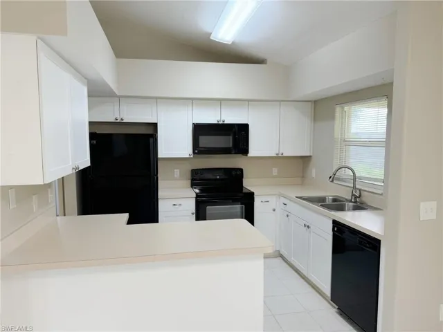 Kitchen featuring kitchen peninsula, vaulted ceiling, light tile flooring, black appliances, and sink