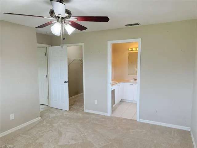 Unfurnished bedroom featuring light carpet, ensuite bathroom, ceiling fan, and a walk in closet