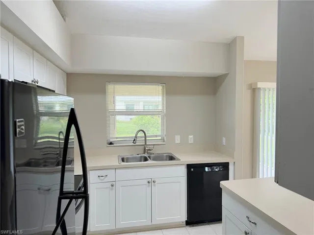 Kitchen with fridge, black dishwasher, light tile floors, sink, and white cabinets