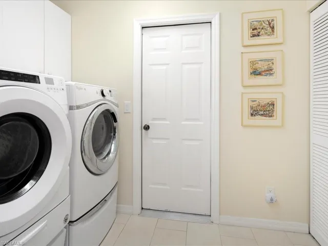 Clothes washing area featuring cabinets, washing machine and clothes dryer, and light tile patterned flooring