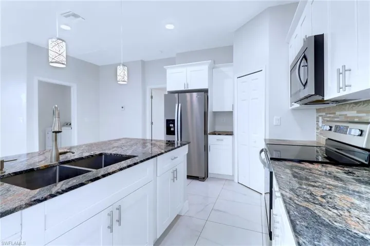 Kitchen featuring appliances with stainless steel finishes, dark stone counters, decorative light fixtures, white cabinets, and decorative backsplash