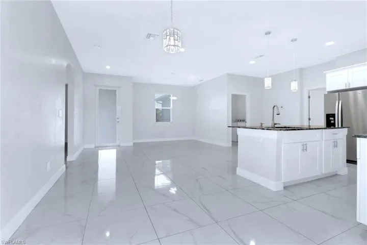 Kitchen with white cabinets, stainless steel fridge with ice dispenser, hanging light fixtures, dark stone countertops, and open floor plan