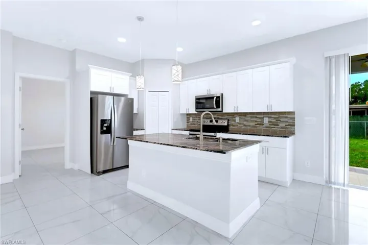 Kitchen with appliances with stainless steel finishes, backsplash, dark stone countertops, decorative light fixtures, and white cabinets