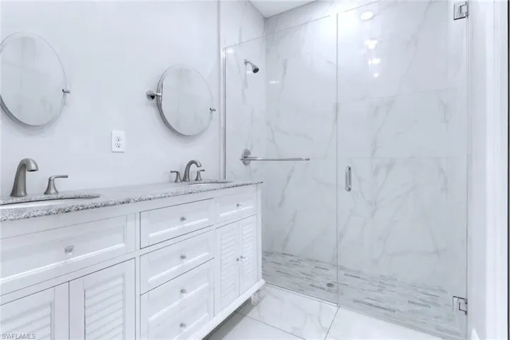 Bathroom with a marble finish shower, light marble finish floors, and double vanity
