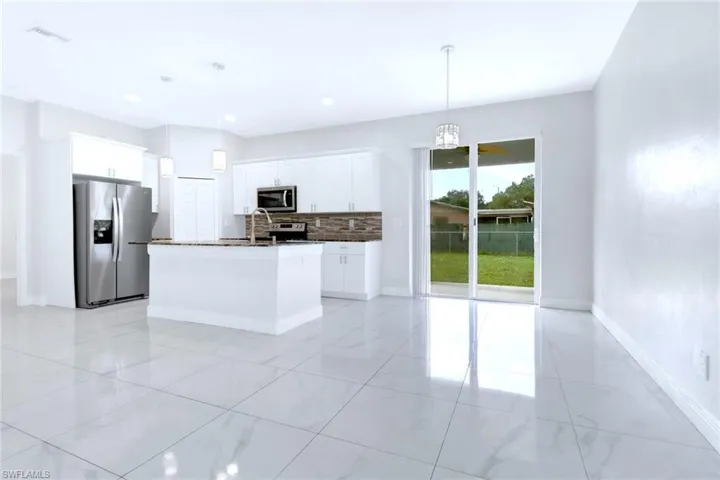Kitchen with tasteful backsplash, appliances with stainless steel finishes, white cabinetry, and pendant lighting