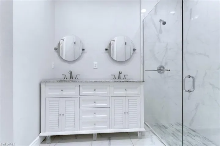 Full bath with a marble finish shower, double vanity, and light marble finish flooring