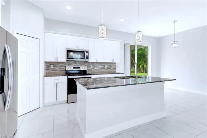 Kitchen with decorative backsplash, dark stone countertops, stainless steel appliances, a center island with sink, and white cabinetry