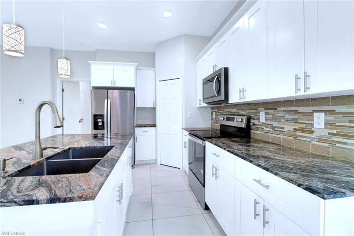 Kitchen featuring appliances with stainless steel finishes, dark stone counters, pendant lighting, white cabinetry, and recessed lighting