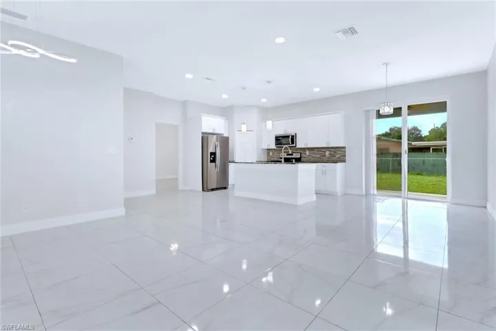 Kitchen with open floor plan, white cabinets, decorative light fixtures, dark countertops, and backsplash