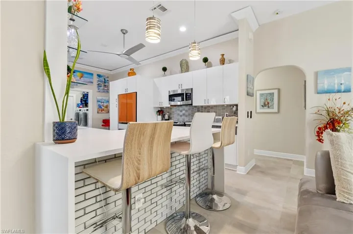 Kitchen with a kitchen bar, decorative backsplash, white cabinets, and decorative light fixtures