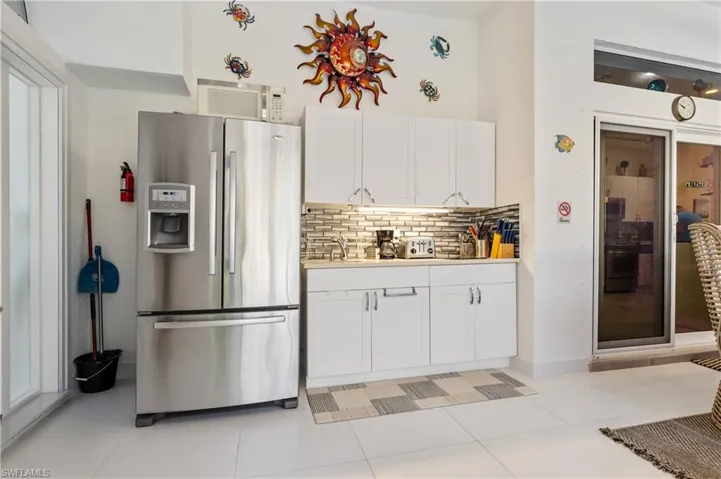 Outdoor kitchen featuring stainless steel refrigerator, white cabinetry, quartz countertop, and ceramic tile floors