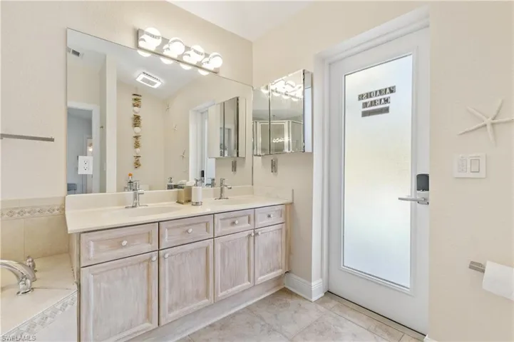 Bathroom with double vanity, light tile patterned floors, and a relaxing tiled tub