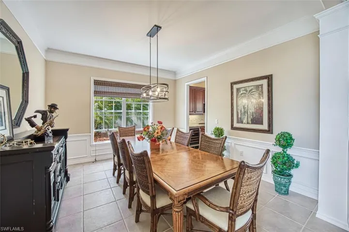 Dining room featuring a wainscoted wall, crown molding, a notable chandelier, light tile patterned floors, and a decorative wall