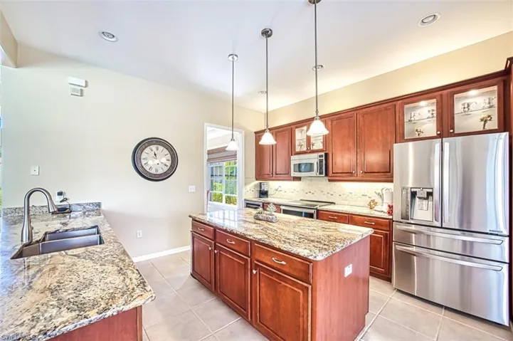 Kitchen featuring light tile patterned floors, stainless steel appliances, tasteful backsplash, a sink, and light stone countertops