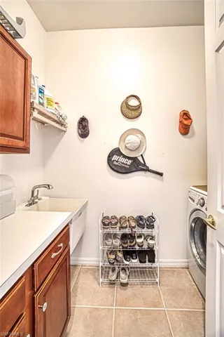 Clothes washing area featuring light tile patterned floors, cabinet space, washer / dryer, and baseboards