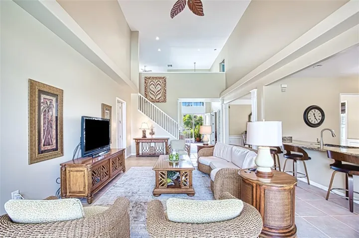 Living area with light tile patterned flooring, a towering ceiling, baseboards, stairs, and a ceiling fan