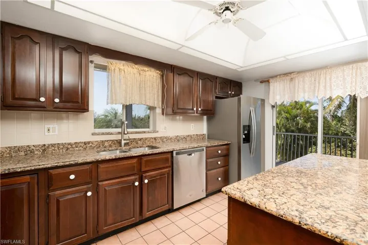 Kitchen featuring light stone countertops, stainless steel appliances, a ceiling fan, a sink, and light tile patterned floors