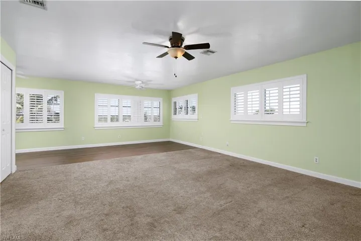 Spare room with baseboards, visible vents, dark colored carpet, and ceiling fan