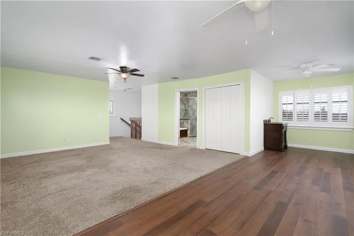 Unfurnished living room featuring a ceiling fan, dark wood-style flooring, baseboards, and visible vents