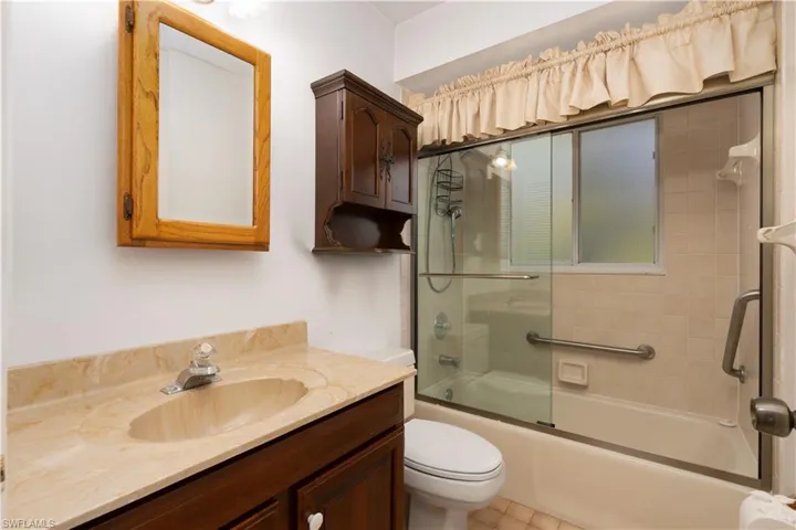 Bathroom with toilet, vanity, and bath / shower combo with glass door