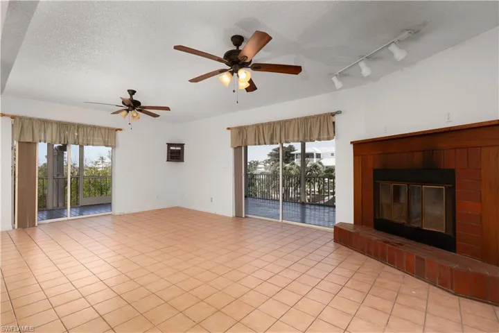 Unfurnished living room with a ceiling fan, a fireplace, a textured ceiling, light tile patterned floors, and baseboards