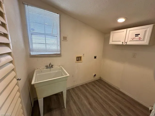 Clothes washing area with electric dryer hookup, washer hookup, dark wood-type flooring, cabinets, and a textured ceiling