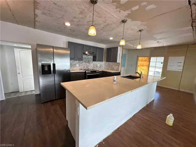 Kitchen featuring a spacious island, backsplash, appliances with stainless steel finishes, and dark hardwood / wood-style flooring