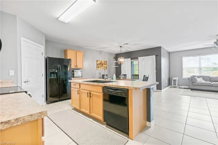 Kitchen featuring black appliances, ceiling fan with notable chandelier, light brown cabinets, sink, and a center island with sink