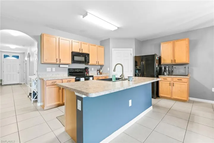 Kitchen featuring light tile patterned flooring, range with electric cooktop, and an island with sink