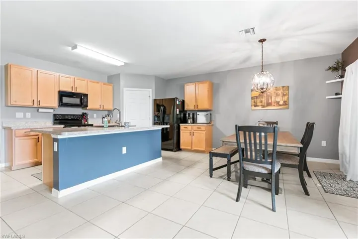 Kitchen with light tile patterned flooring, black appliances, light brown cabinetry, and an island with sink