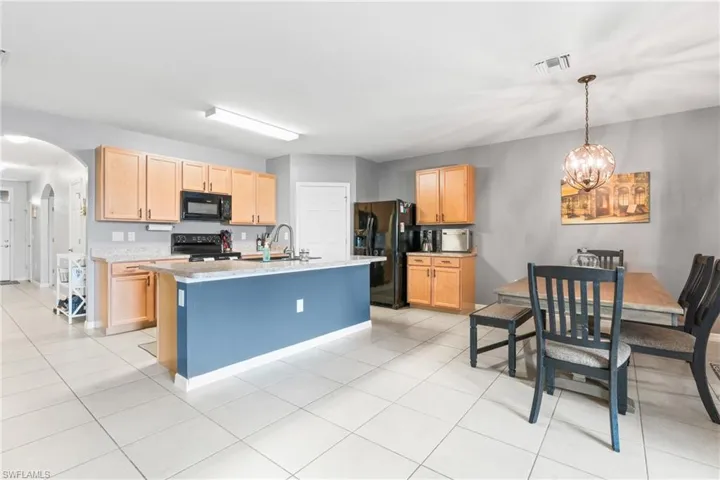 Kitchen featuring a center island with sink, black appliances, light brown cabinets, and light tile patterned floors