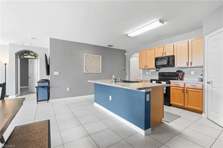 Kitchen featuring sink, black appliances, light tile patterned floors, and an island with sink