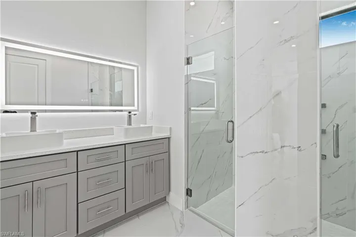 Bathroom with double vanity, a marble finish shower, and light marble finish floors