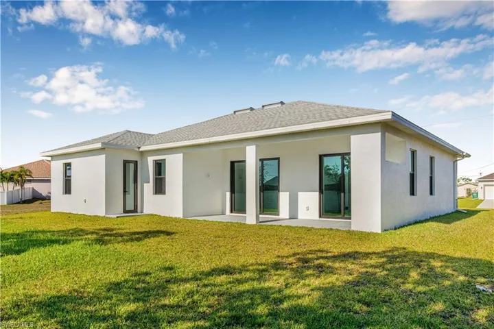 Rear view of property featuring a lawn, stucco siding, a patio area, and a shingled roof