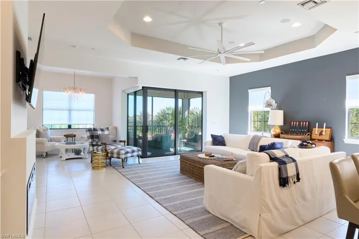 Living room featuring a tray ceiling, a ceiling fan, recessed lighting, light tile patterned flooring, and a chandelier
