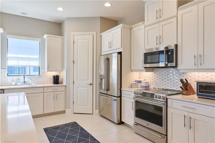 Kitchen with stainless steel appliances, white cabinets, light tile patterned flooring, backsplash, and recessed lighting