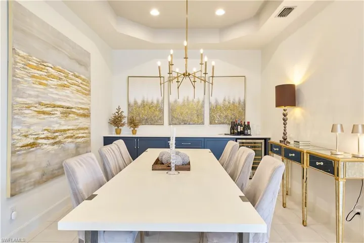 Dining space featuring a tray ceiling, a chandelier, recessed lighting, light tile patterned flooring, and wine cooler