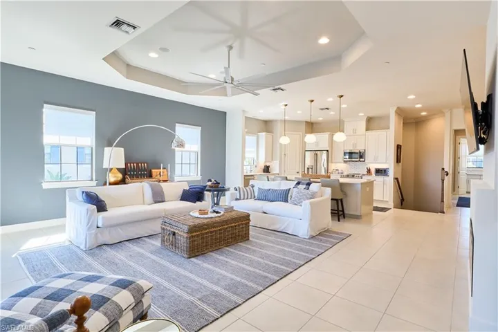 Living area with plenty of natural light, a ceiling fan, a tray ceiling, light tile patterned floors, and recessed lighting