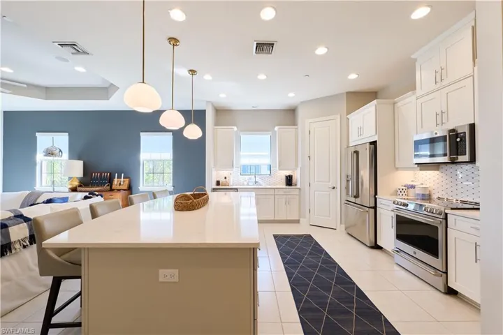 Kitchen featuring open floor plan, appliances with stainless steel finishes, a breakfast bar area, white cabinets, and hanging light fixtures