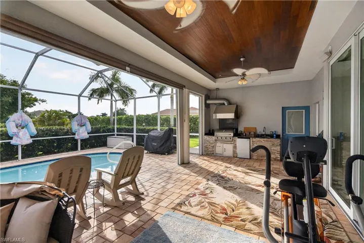 Expansive screened patio with a built-in outdoor kitchen, wood-finish ceiling, and ceiling fans