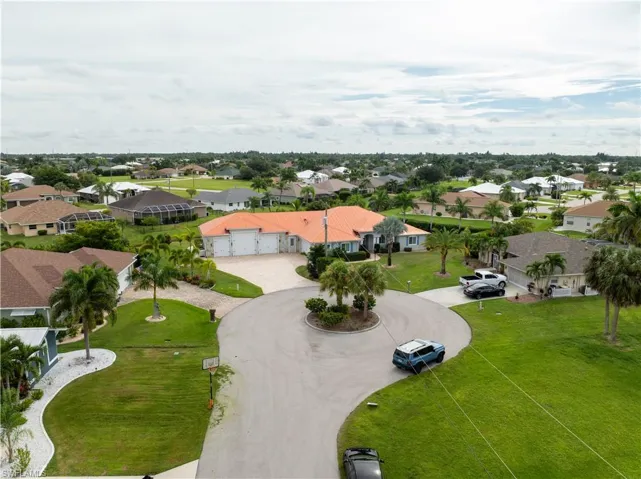 Aerial view of a residential neighborhood with verdant landscaping, mature palm trees, and multiple single-story homes featuring distinct roofing styles