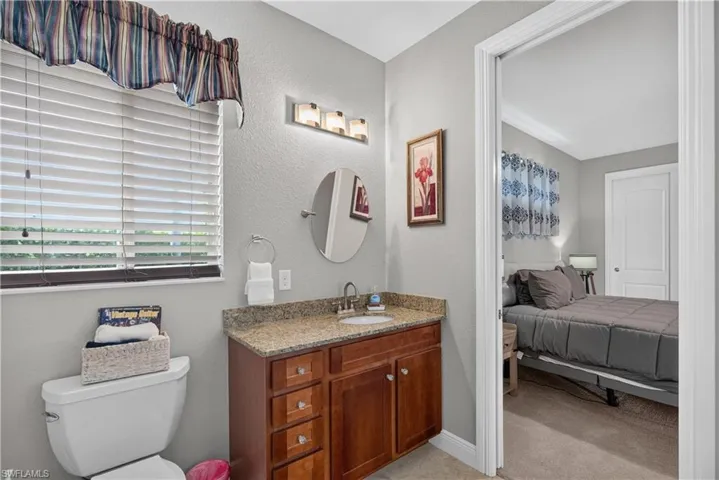 Vanity with a granite countertop, wood-finish cabinetry, and a round mirror