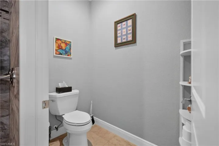 Light-colored wall finish, built-in shelving, tile flooring, and a white toilet