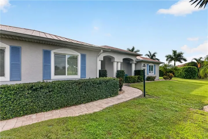Stucco exterior with blue decorative shutters, covered entry with columns, and a paver pathway