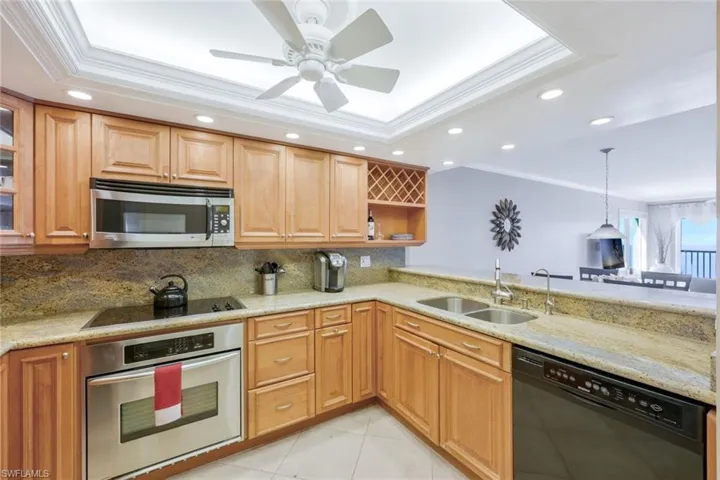 Kitchen featuring ornamental molding, a tray ceiling, black appliances, sink, and tasteful backsplash